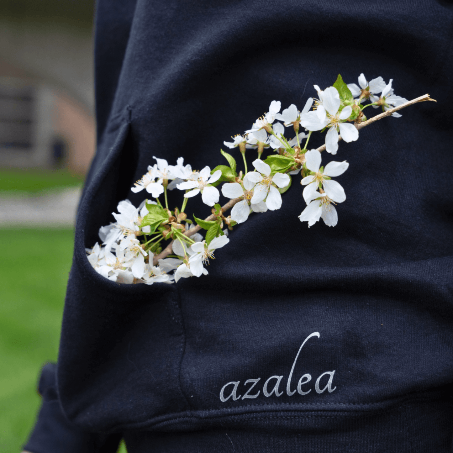 A black Azalea brand hoodie with a pocket overflowing with white blossoms, showcasing the brand's connection to natural beauty and comfort. The subtle essential oil infusion enhances the sensory experience, providing a gentle, perfume-inspired scent for everyday wear