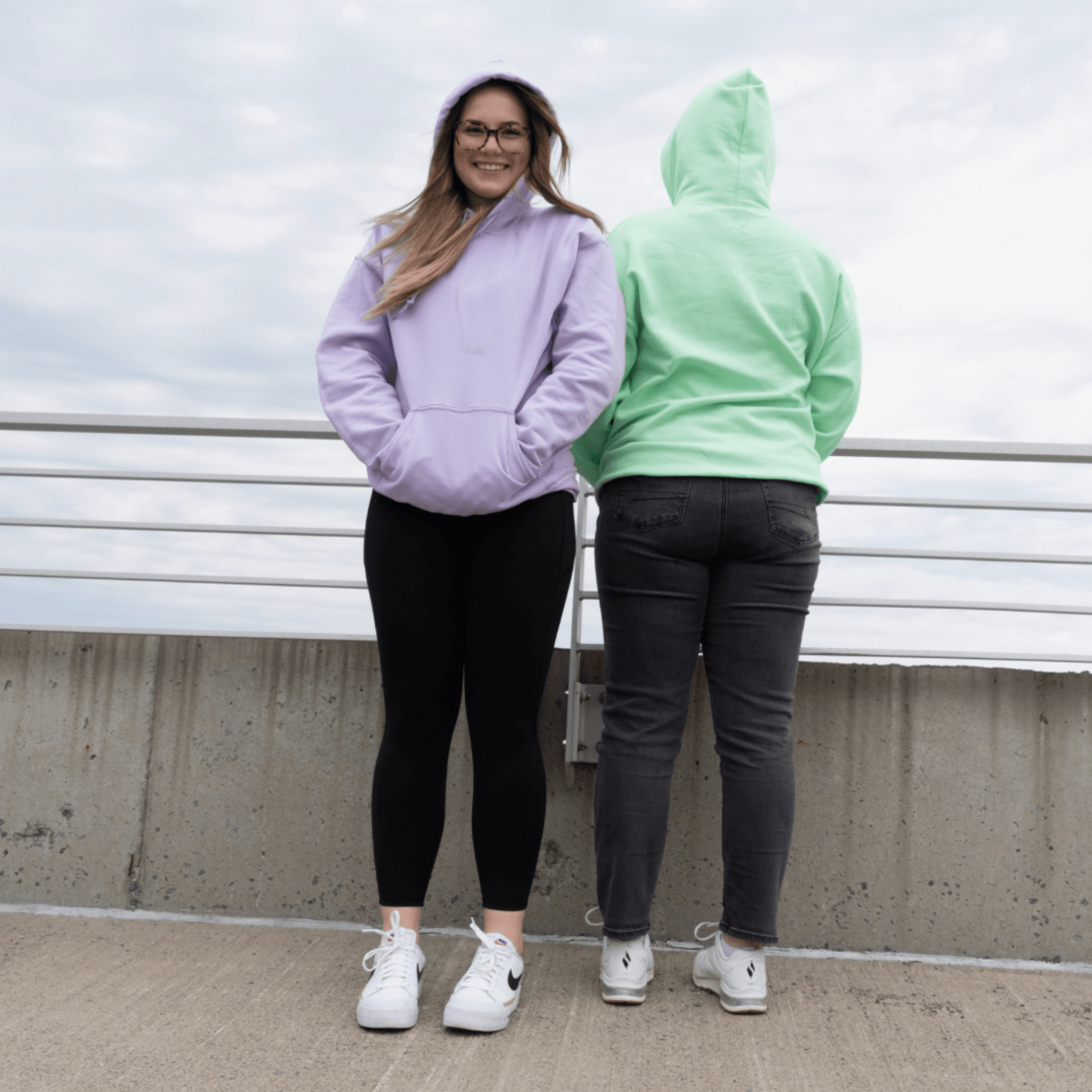 Front and back view of individuals wearing soft Azalea brand essential oil-infused comfort hoodies in lavender and mint, paired with leggings and jeans, by a scenic overlook. These hoodies enhance daily scenes with their gentle aromatic presence, creating a serene, perfume-like ambiance for active or relaxed moments