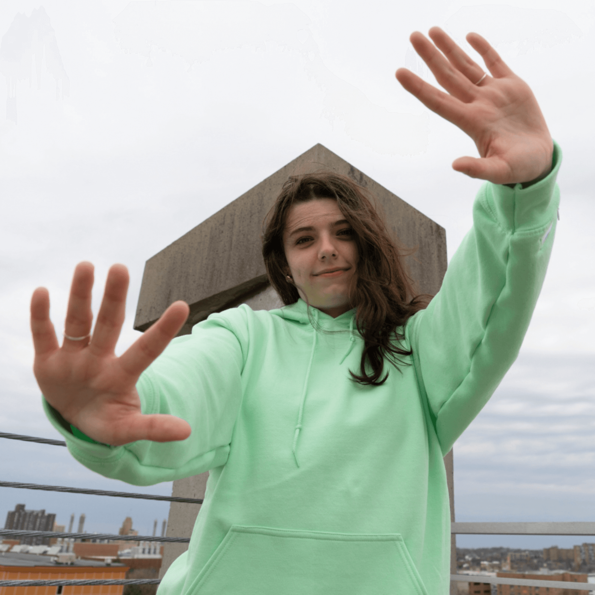 Smiling individual wearing a soft mint green Azalea brand comfort hoodie, captured on an urban rooftop. Infused with natural essential oils, this aromatic apparel offers a fresh, calming scent, creating a unique sensory experience that elevates everyday scenes and promotes a feeling of well-being